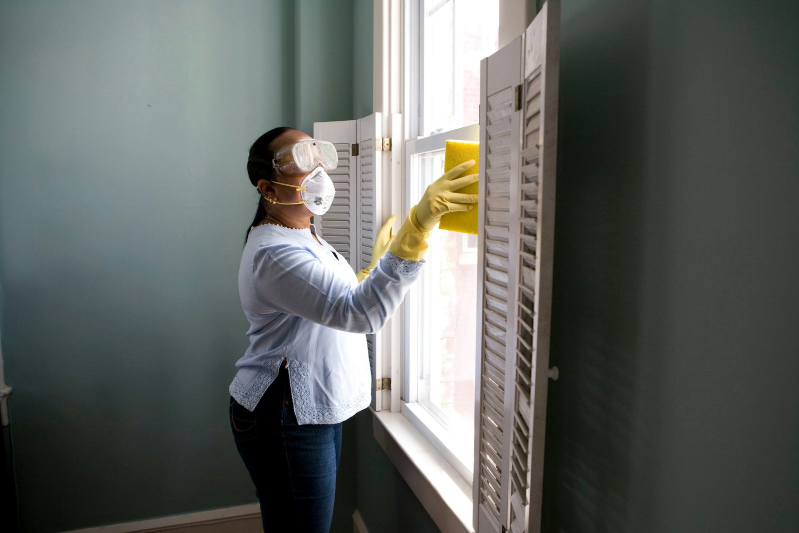Cleaner in gloves and mask wiping a window